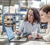Two women are looking at a laptop together inside of a warehouse
